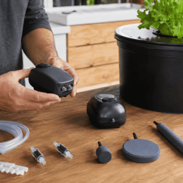 Persona comparando bombas de aire, tubos, válvulas y diferentes piedras difusoras junto a un sistema DWC doméstico