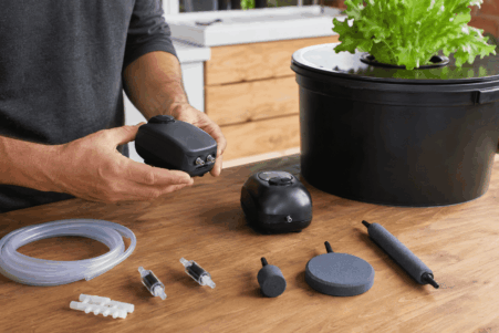 Persona comparando bombas de aire, tubos, válvulas y diferentes piedras difusoras junto a un sistema DWC doméstico